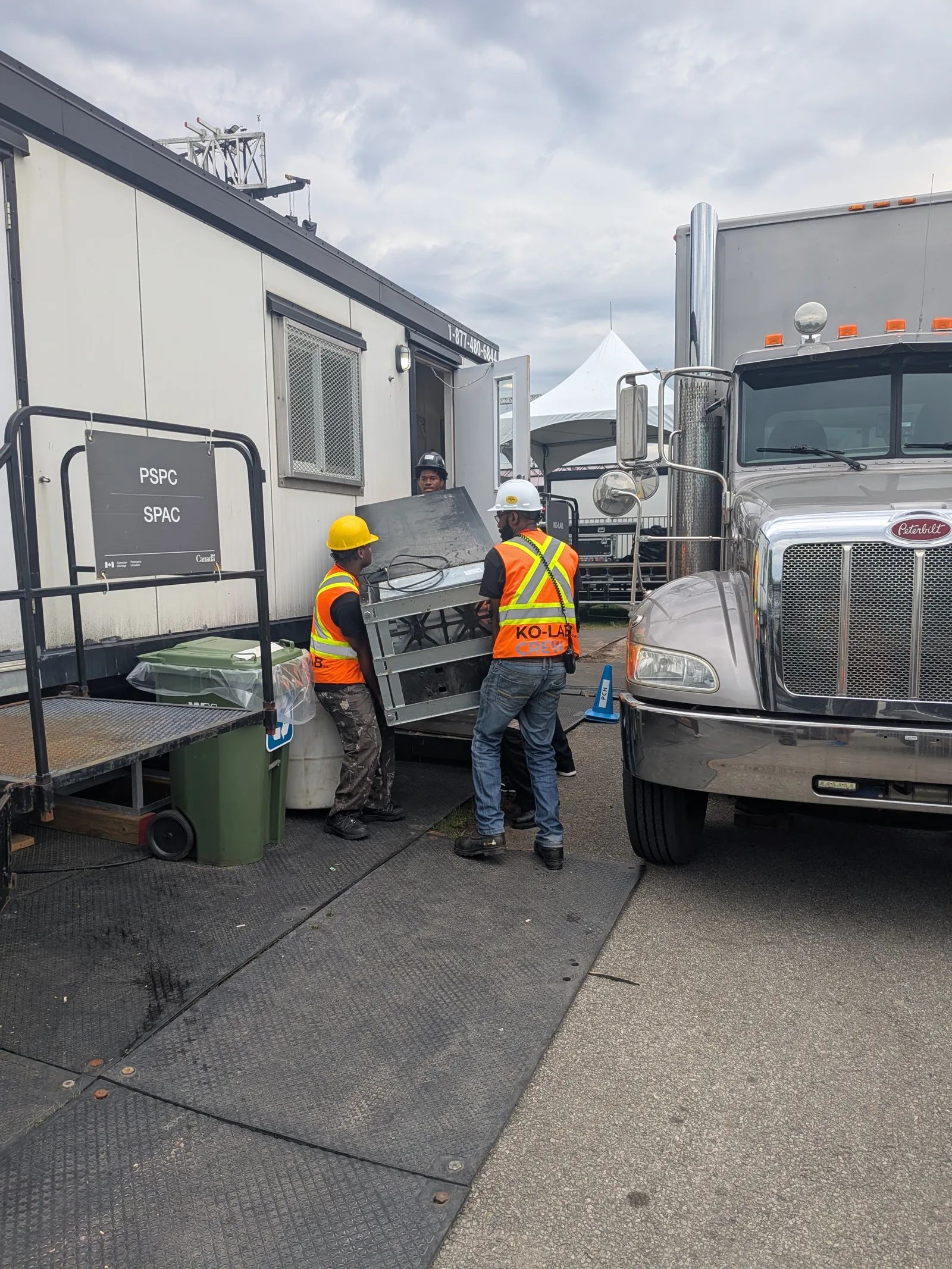 Deux membres de l’équipe KO-LAB, casques et gilets de sécurité, déchargent un équipement d’un camion