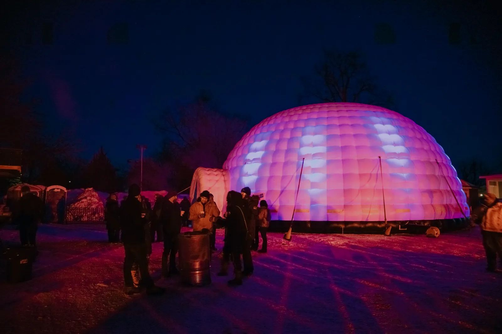 Dôme gonflable illuminé en rose la nuit, avec des visiteurs devant