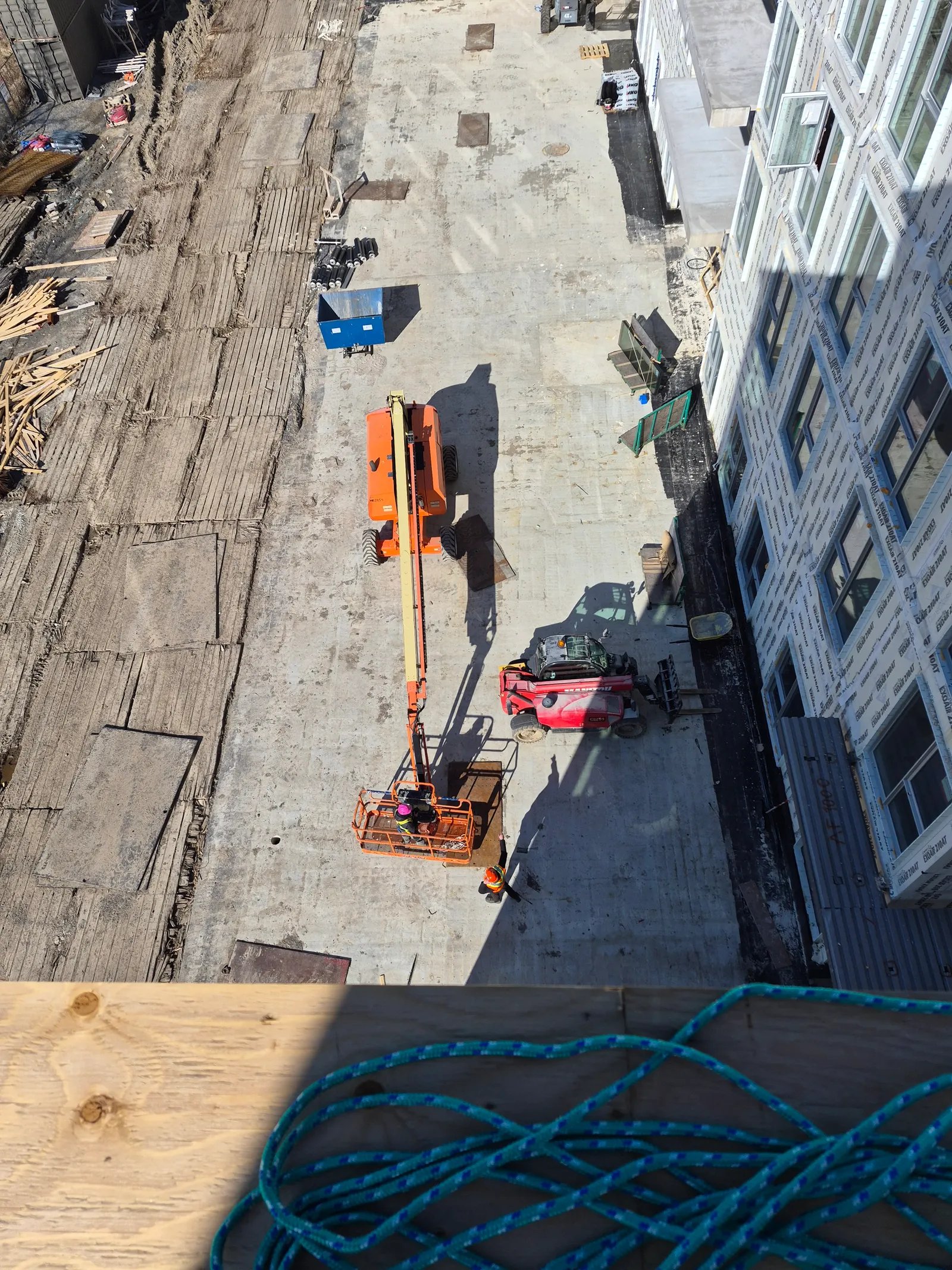 Vue aérienne d’un chantier : nacelle articulée orange et véhicules le long d’un immeuble