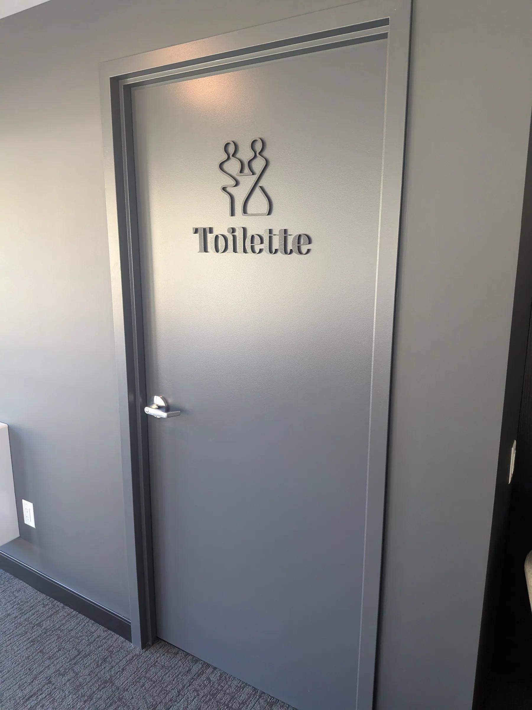 Pictogramme et lettrage 3D « Toilette » sur une porte grise