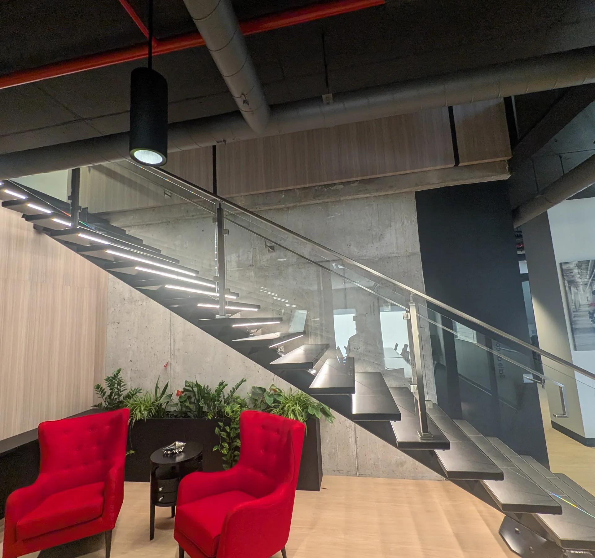 Escalier en bois et béton avec deux fauteuils rouges dans un hall