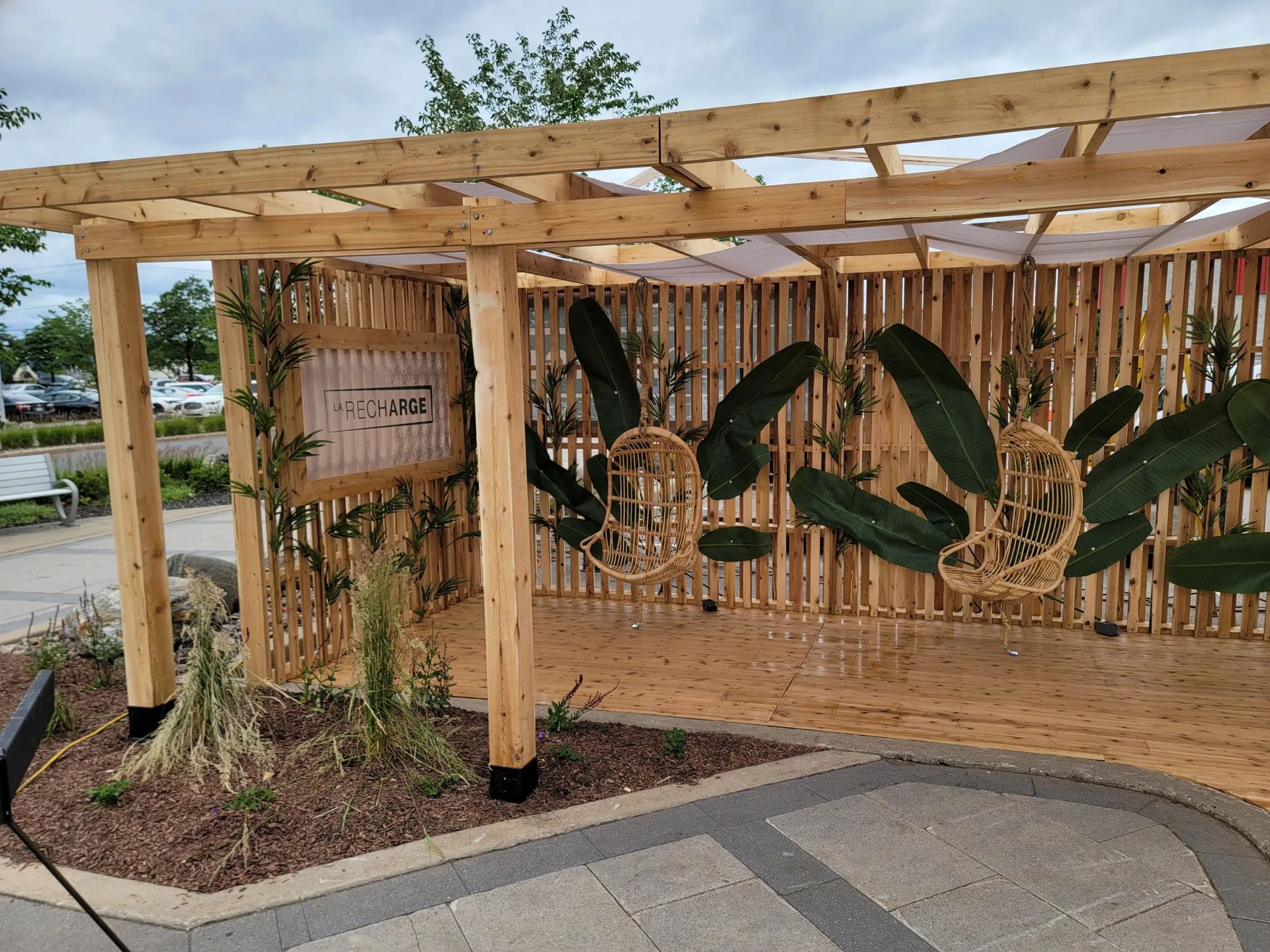 Pergola en bois avec toile, plantes et tables sur une terrasse commerciale