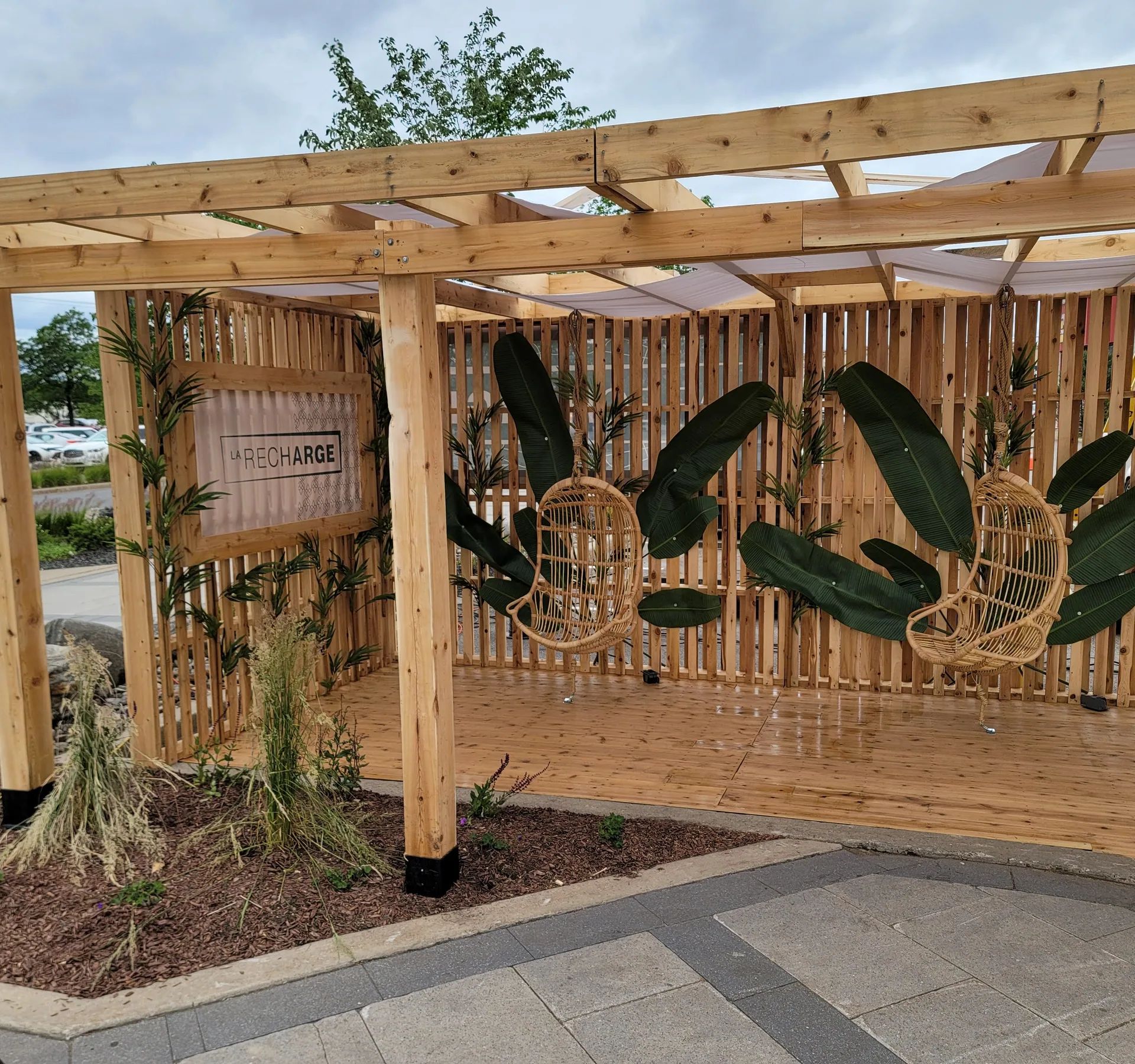 Pergola en bois avec toile, plantes et tables sur une terrasse commerciale