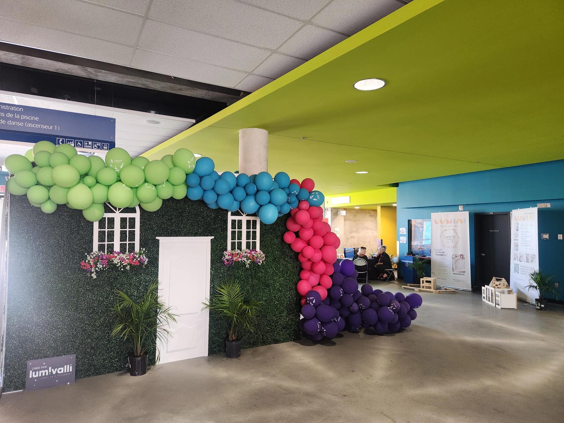 Arche de ballons multicolores autour d’une façade décorative dans un hall sportif
