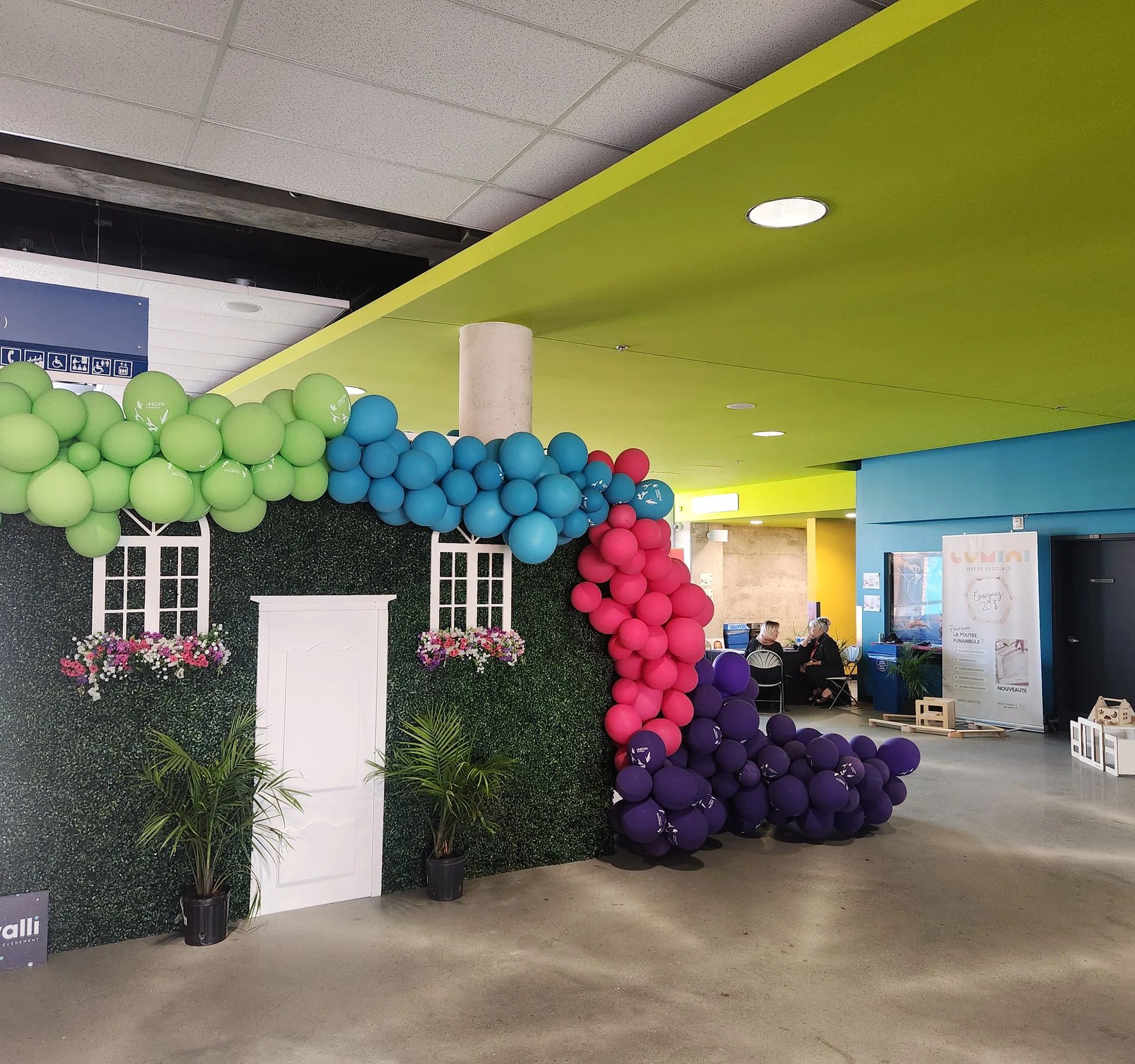 Arche de ballons multicolores autour d’une façade décorative dans un hall sportif